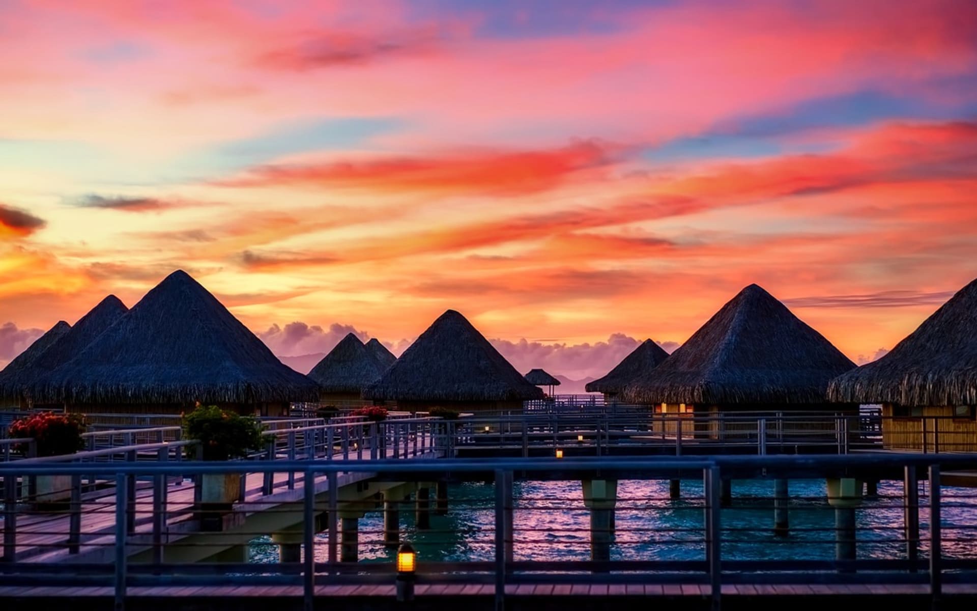 The sun has set, cascading orange and yellow hues across the sky, and the overwater villas are purple. 
