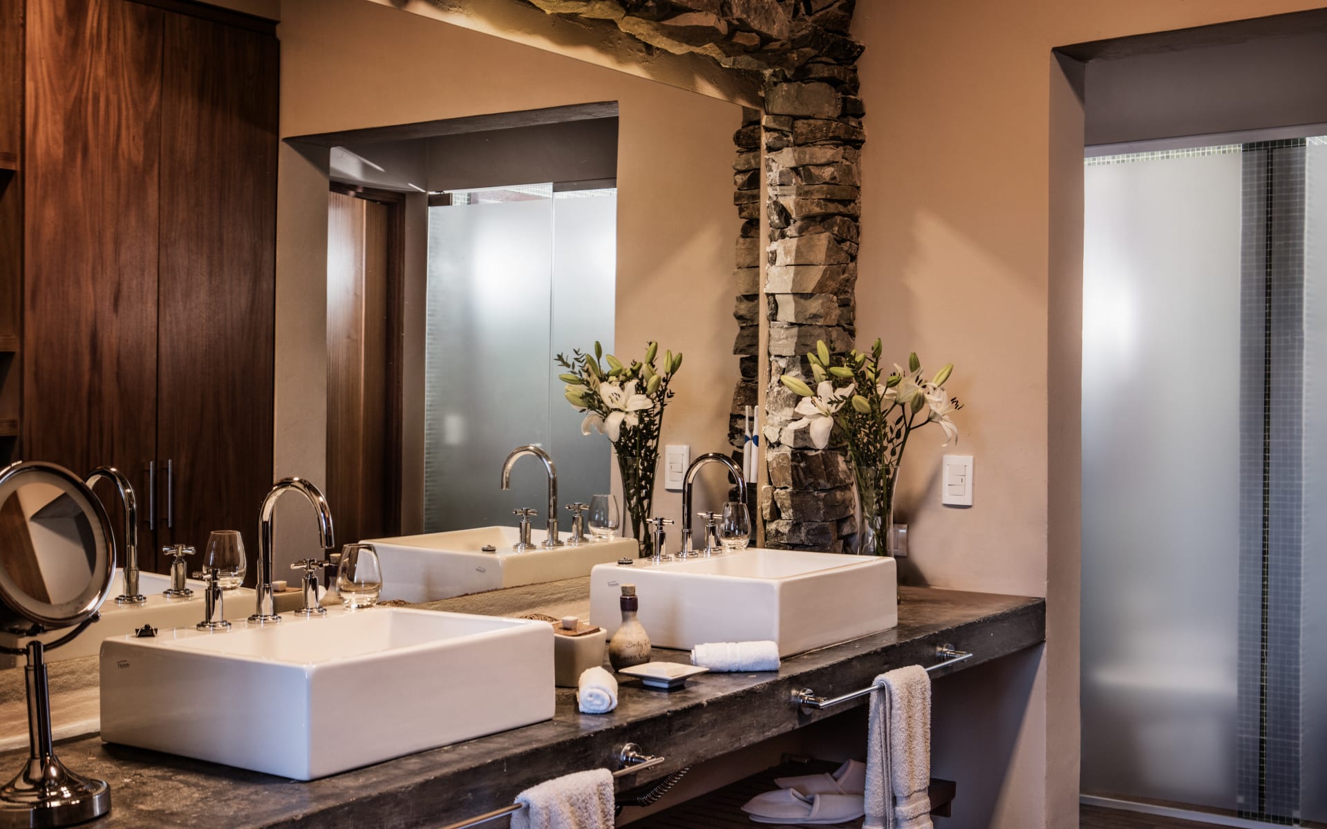 The bathrooms at Canvas Wine Lodge have dual sinks, surrounded by a large mirror and flowers.