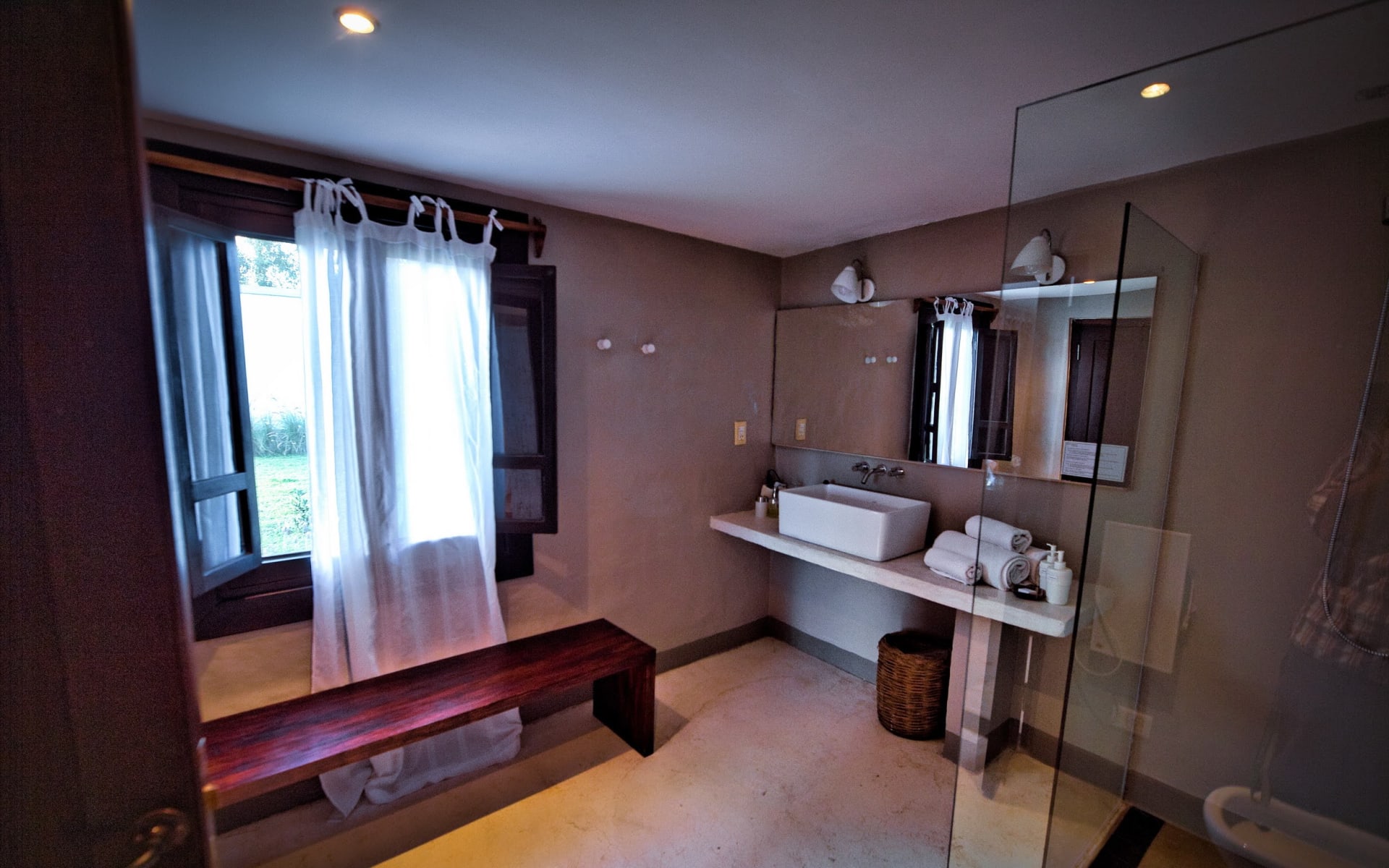 The bathrooms at Finca Valentina are spacious, with a bench, a walk-in shower and a sink with towels and a mirror.