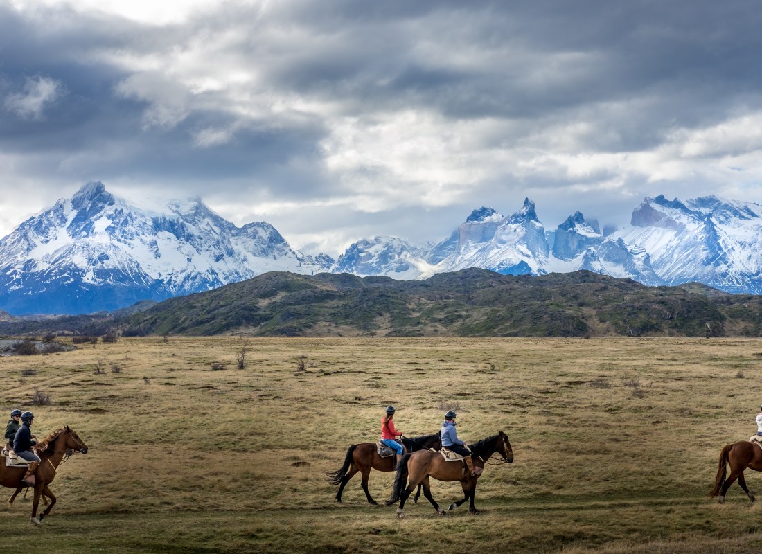 A group of people horse riding on a field with a background of a snow-capped mountain in Torres del Paine, Chile.