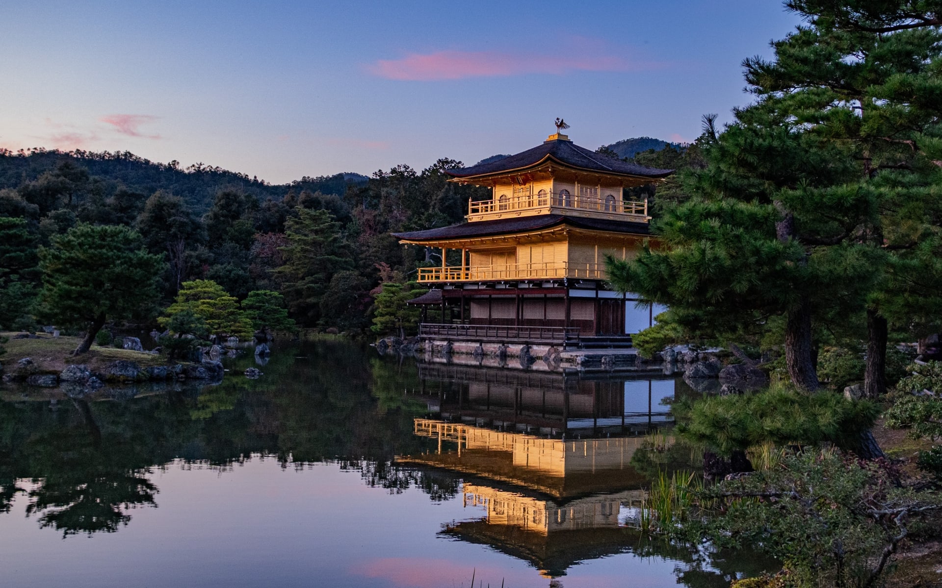 A traditional building in Kyoto is reflected in a lake and surrounded by trees. 