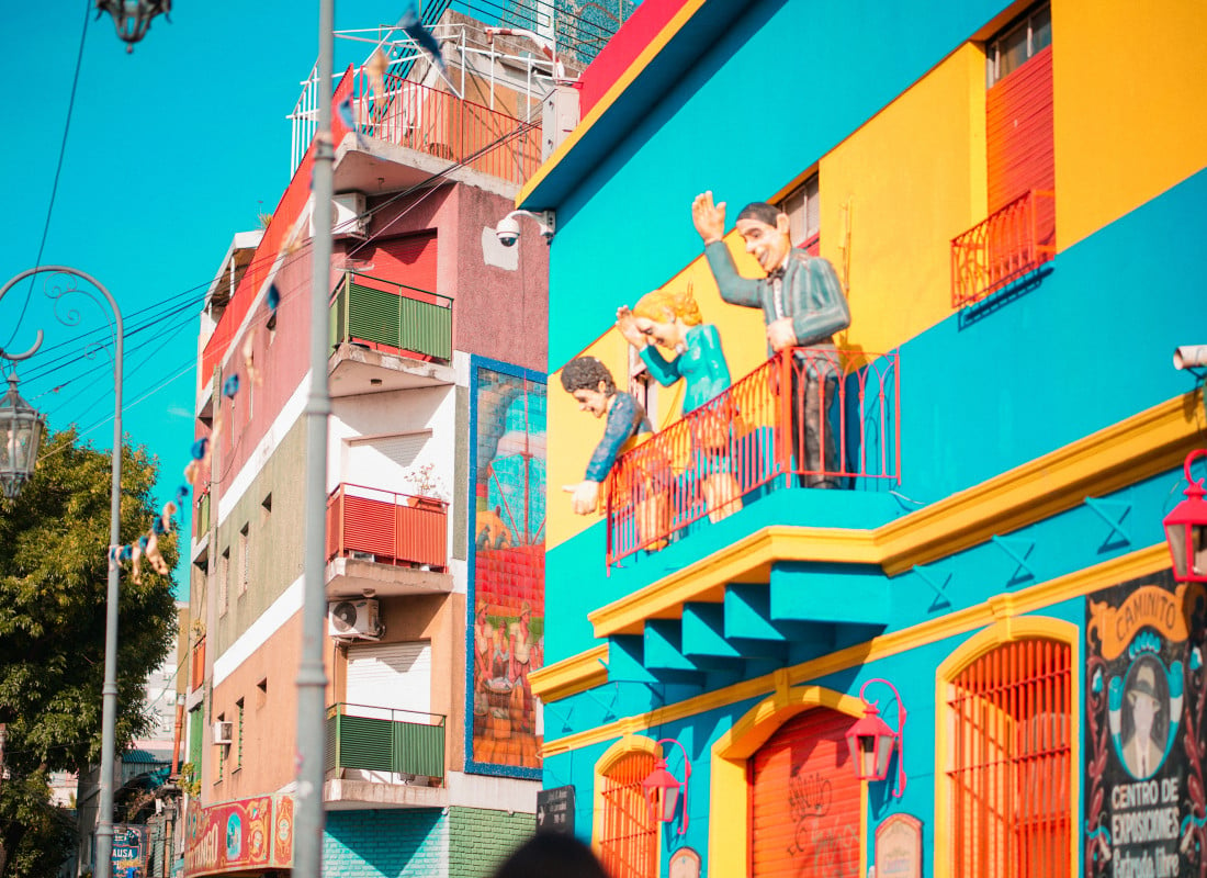 Large animated figurines of humans are standing on a balcony of a multi-coloured building in La Boca, Buenos Aires, Argentina. 