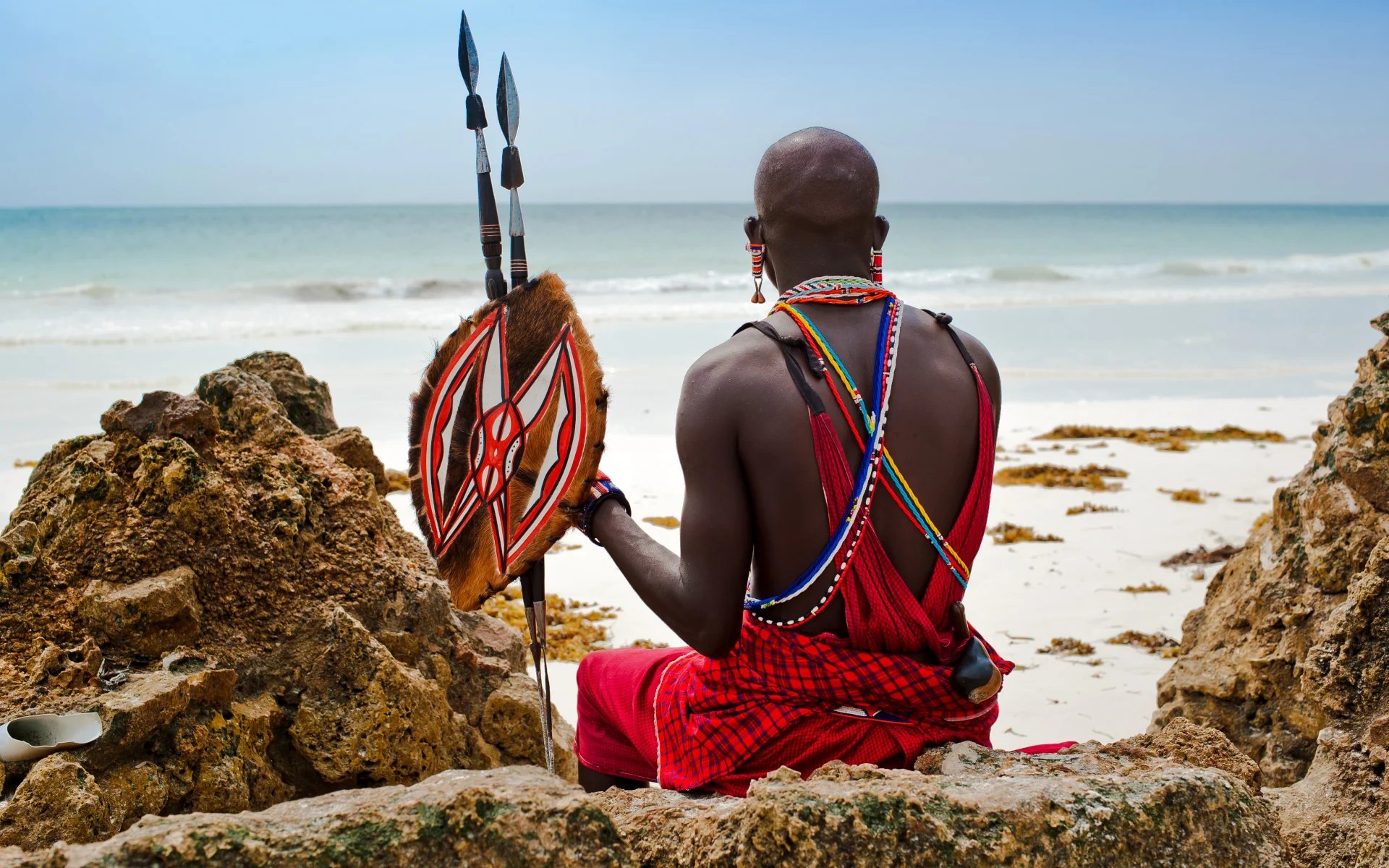 A Maasai Warrior sits on Diani Beach and admires the ocean view.