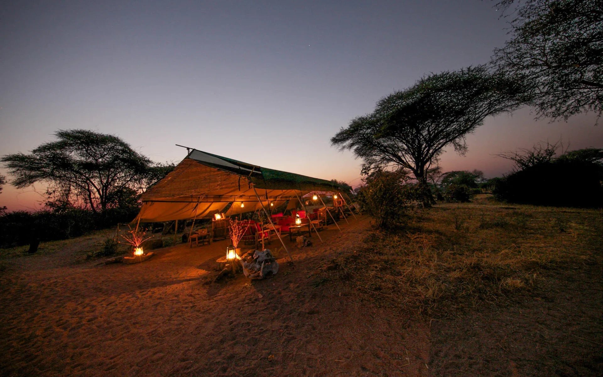 The communal tent is lit up by lamps and candles during the early evening at Mdonya Old River Camp as the sky is filled with soft blues and pinks.