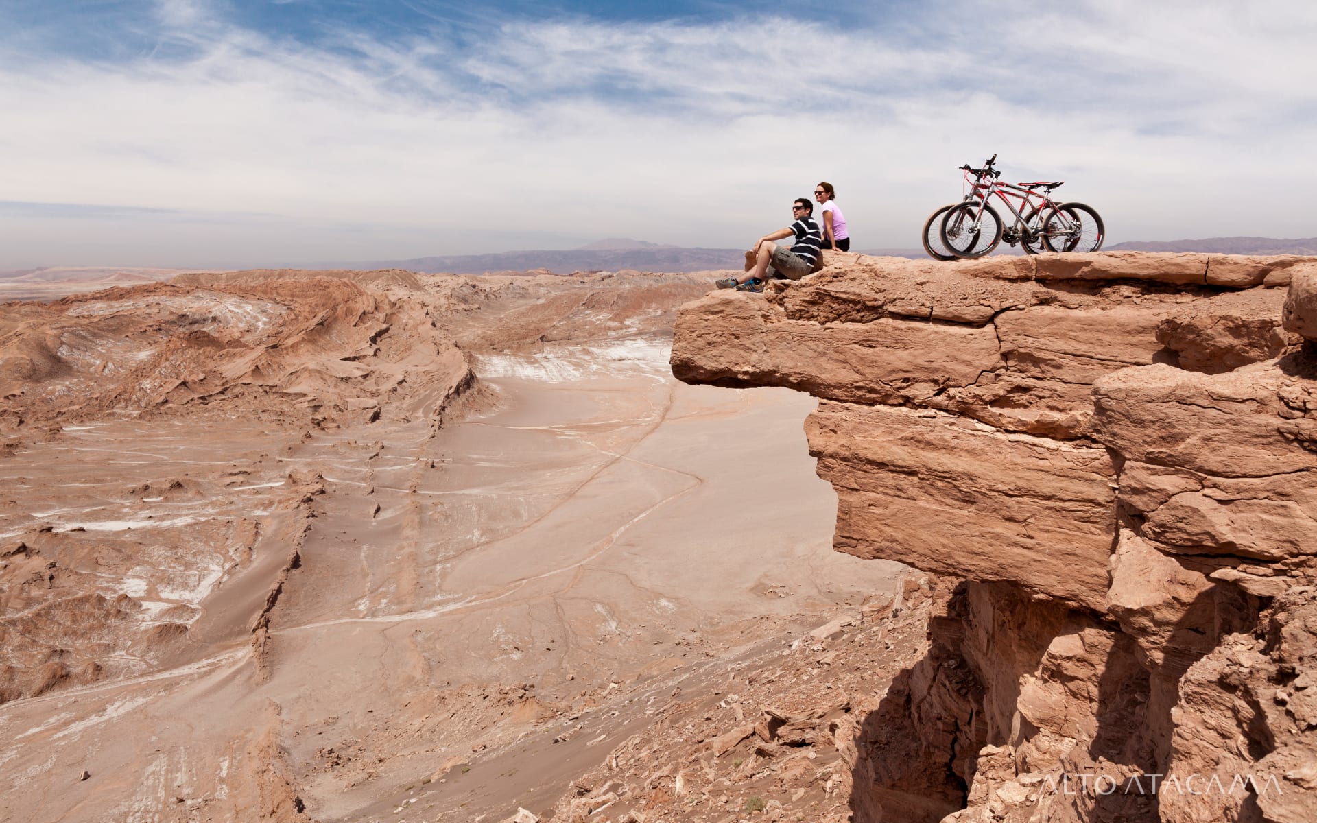 A couple are sitting on a rocky outcrop with bikes.