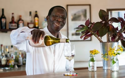 A barman is pouring a glass of white wine over the counter. 