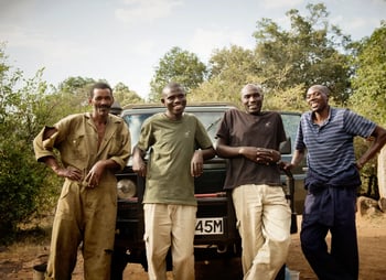 A group of local guides lean against a 4x4 safari vehicle, smiling at the camera.