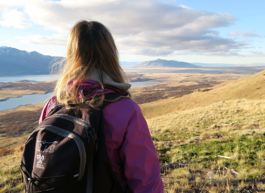 A woman in a purple raincoat and sporting a black backpack is hiking through the Patagonian landscape. 