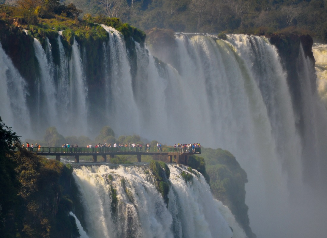 A looking platform is positioned over the waterfalls at Iguazu Falls, and there are lots of people standing there. 

