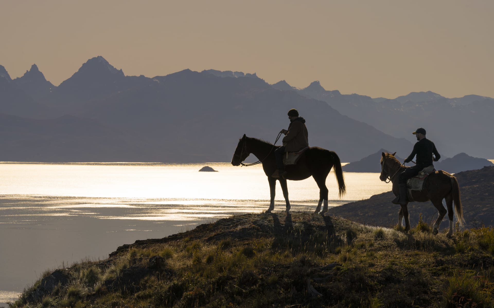 A couple are horseriding near a lake. 