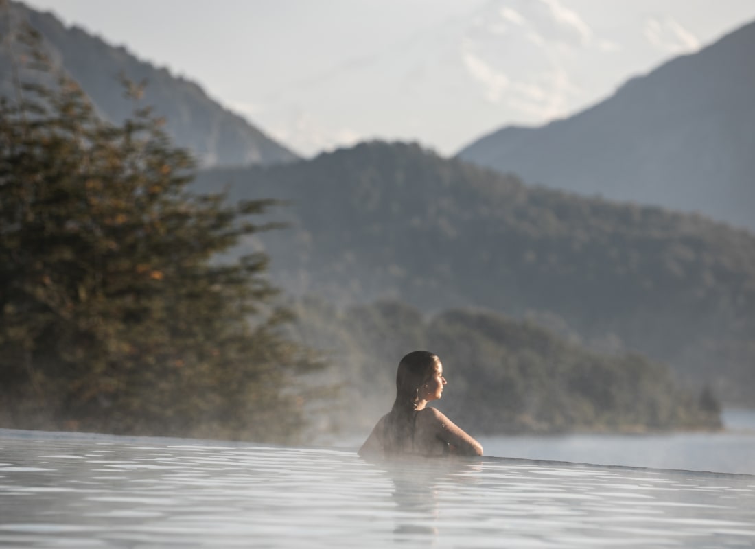 A woman is in an infinity pool looking out to the mountainous distance. 