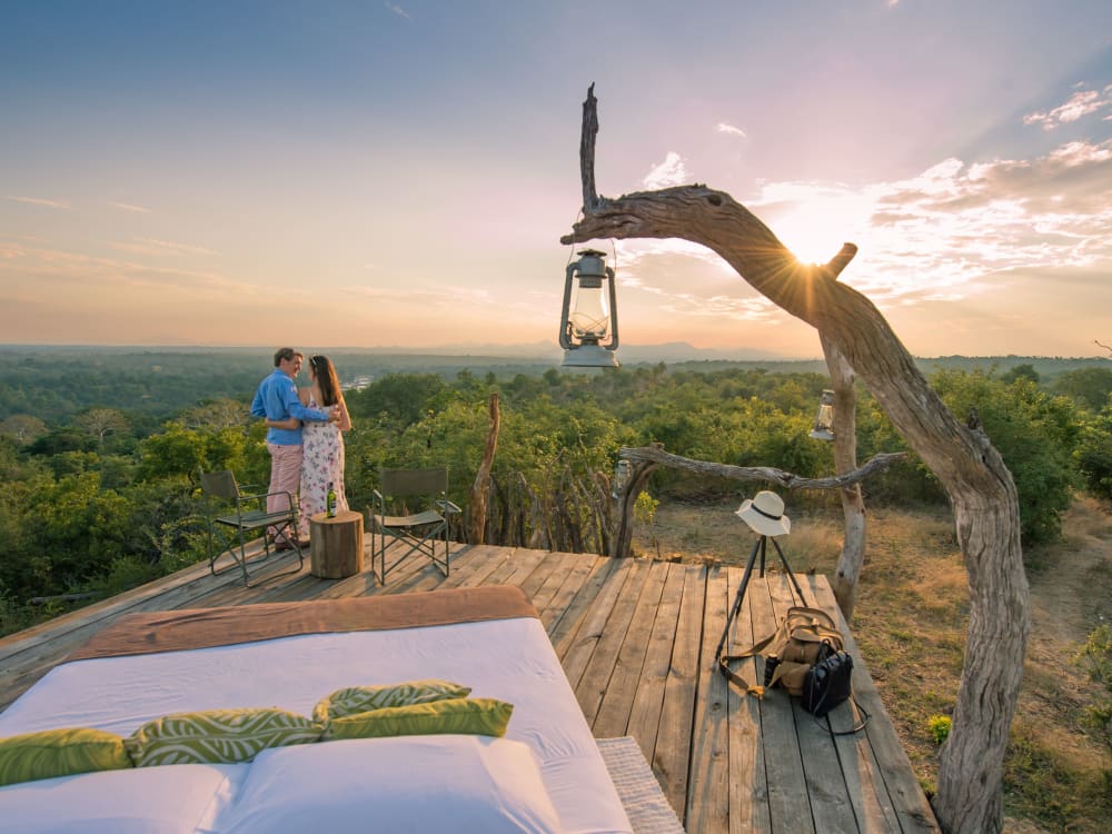 A couple stands on a sleeper deck, watching the sun set over Malawi's countryside.