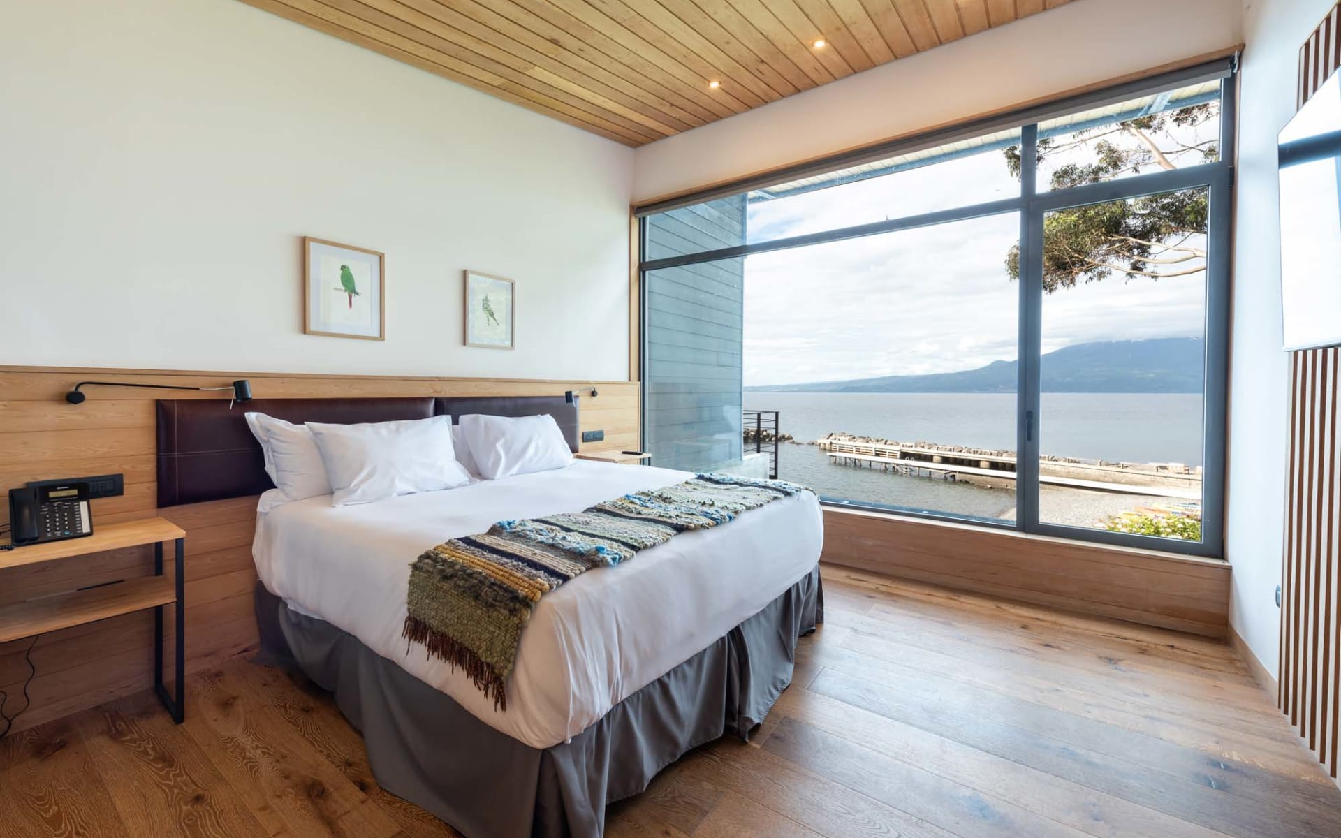 A double bed sits beside a large window overlooking the pier and lake. 