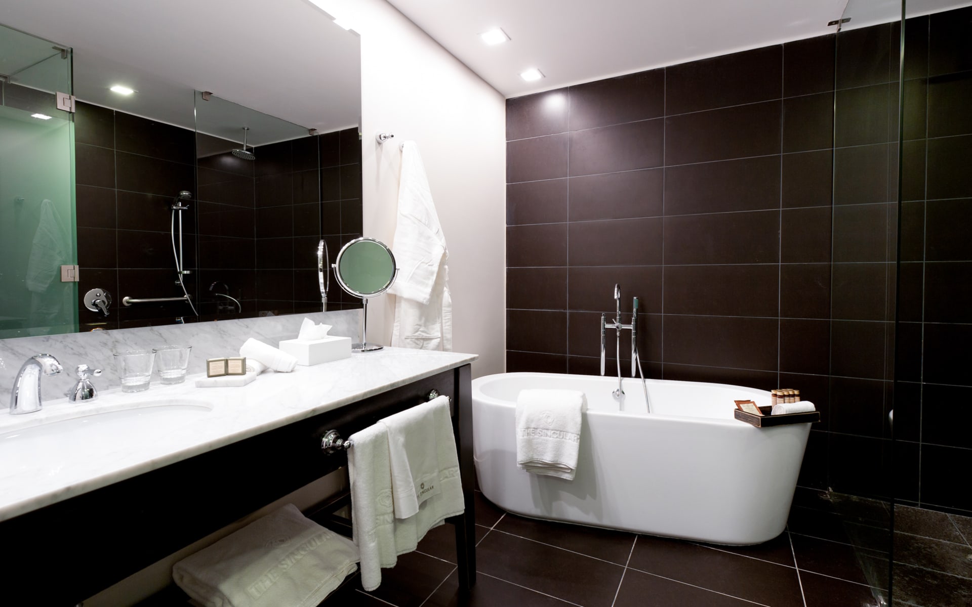 A deep bathtub is in a black and white bathroom with a large mirror and sink. 
