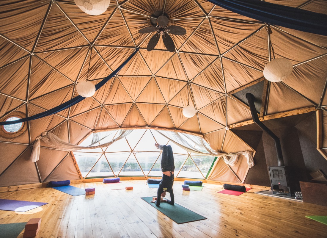 Inside an airy dome, a woman is doing yoga on a yoga mat. 
