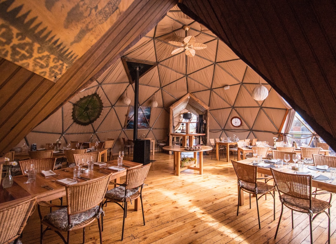 Inside an airy dome is a restaurant with wooden tables, chairs and flooring. 
