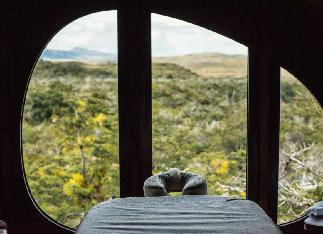 A massage table sits in front of a window with the Patagonian wilderness outside. 