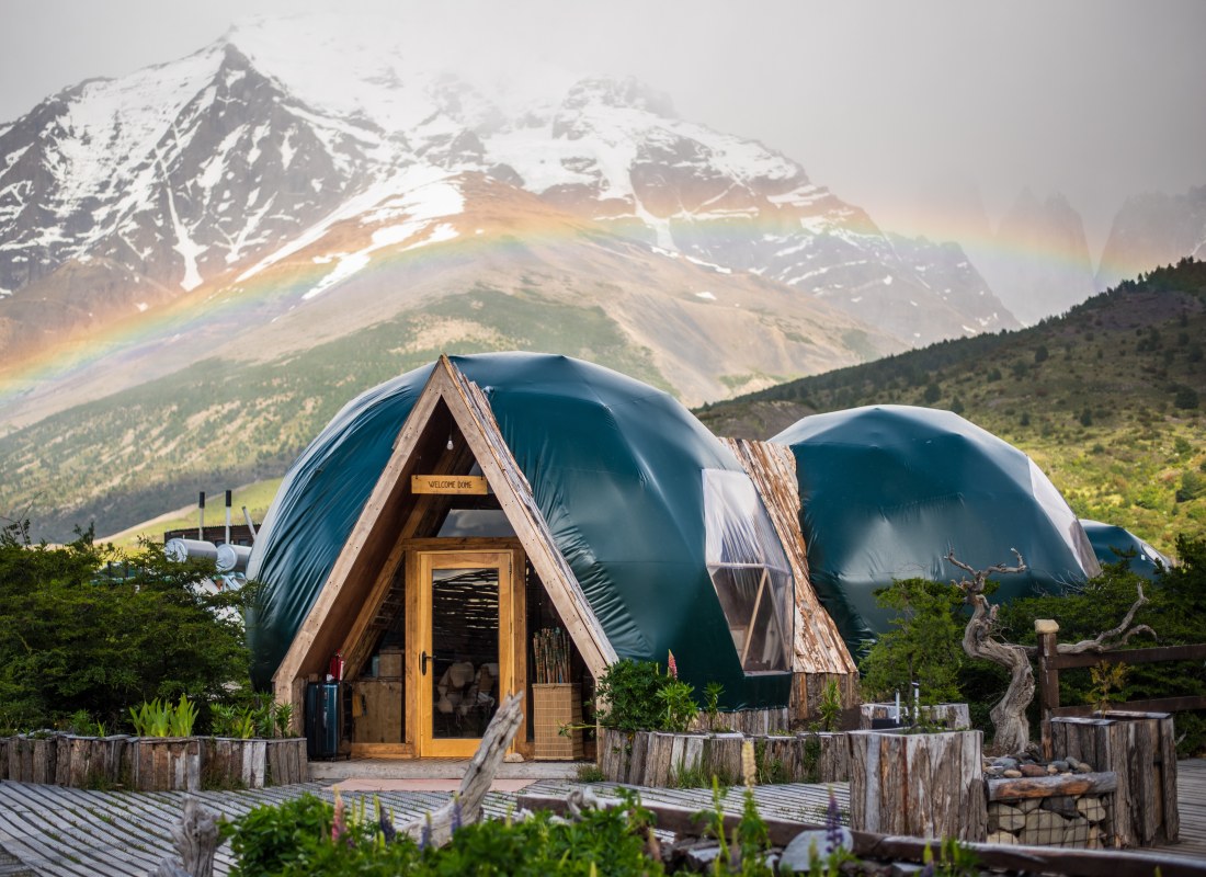 The entrance dome at EcoCamp Patagonia has snowy mountains in the background and a rainbow above. 