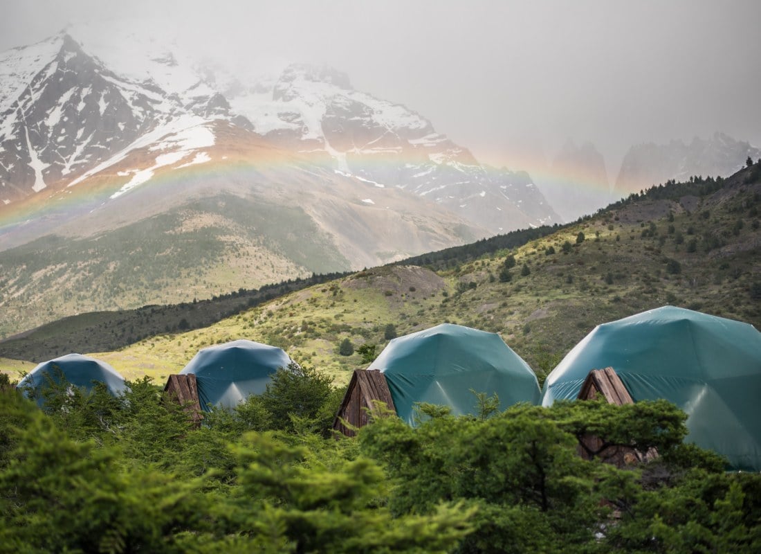 Domes are hidden in the mountainside, covered in snow and have a rainbow. 