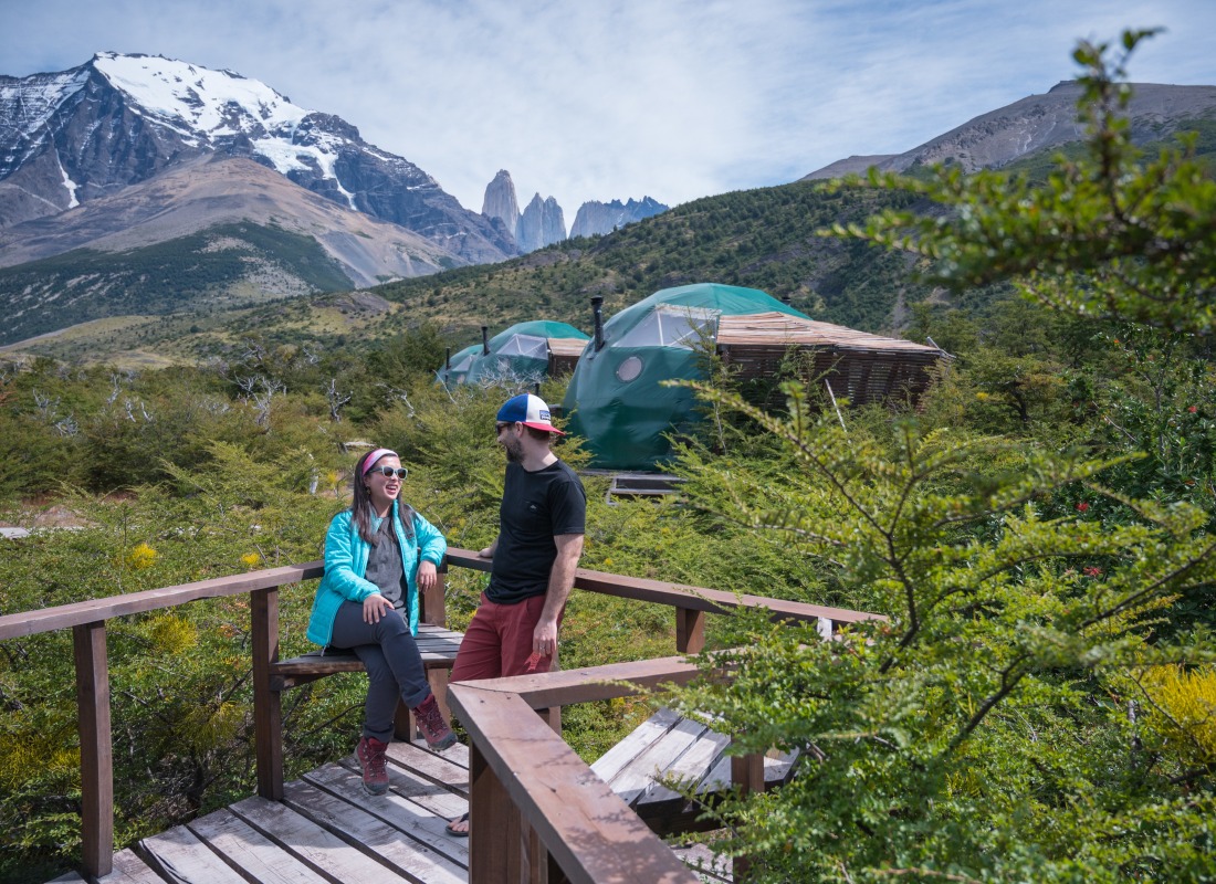 Two people are sitting on a terrace in front of the domes at EcoCamp.
