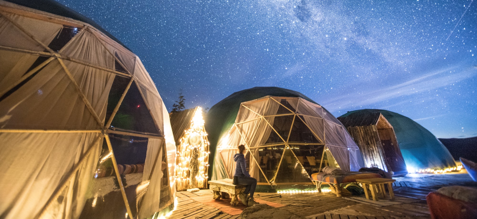 Three domes are illuminated with lights and sit under a starry night. 