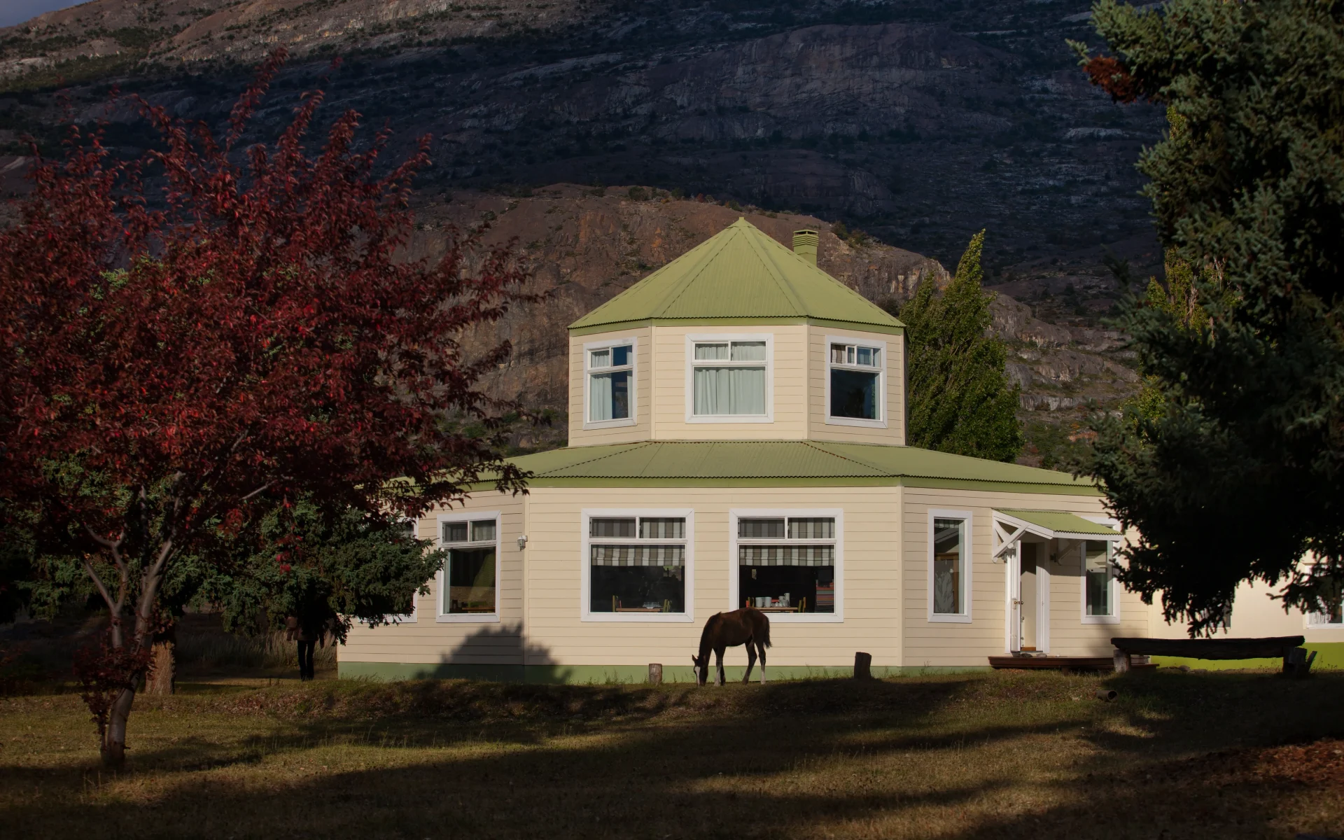The architecture of Estancia Cristina is octagonal with green roofing. A horse stands ahead of the building besides autumnal trees.