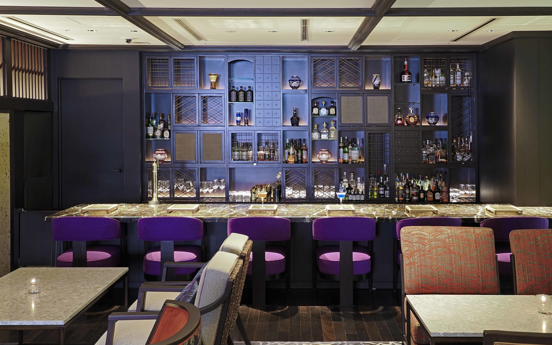 The bar at Dhawa Yura Hotel in Kyoto has purple sears, many tables and shelves of alcohol. 