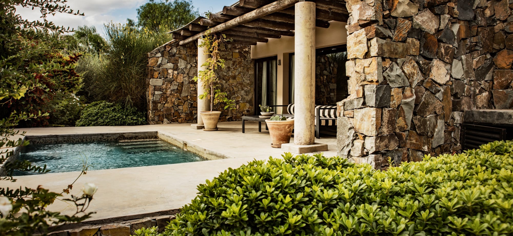 Canvas Wine Lodge Village is a stone building with two outdoor columns overlooking a pool and shrubbery. 