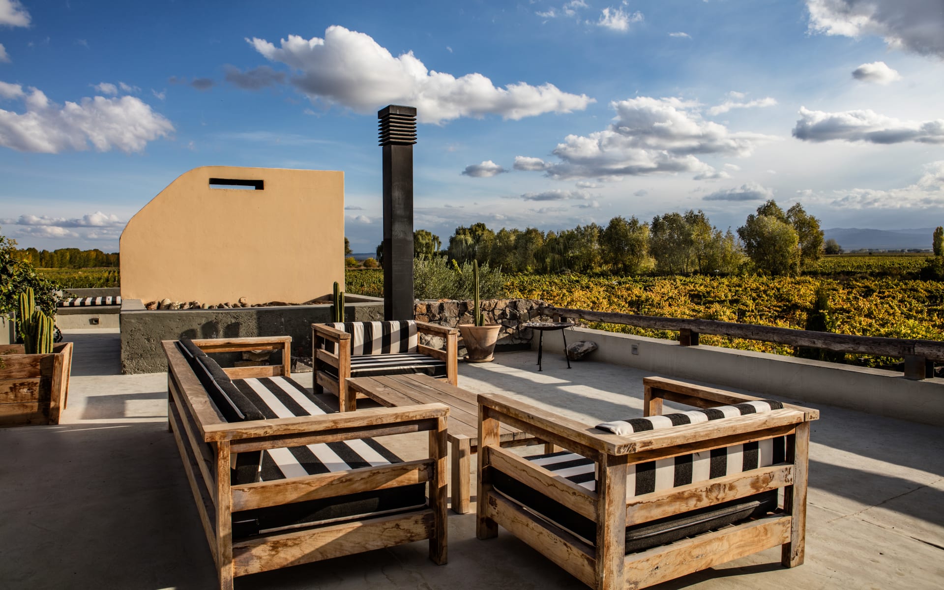 On the roof of Canvas Wine Lodge is a seating area with large wooden chairs, black and white pillows, and an outdoor cooking area. 