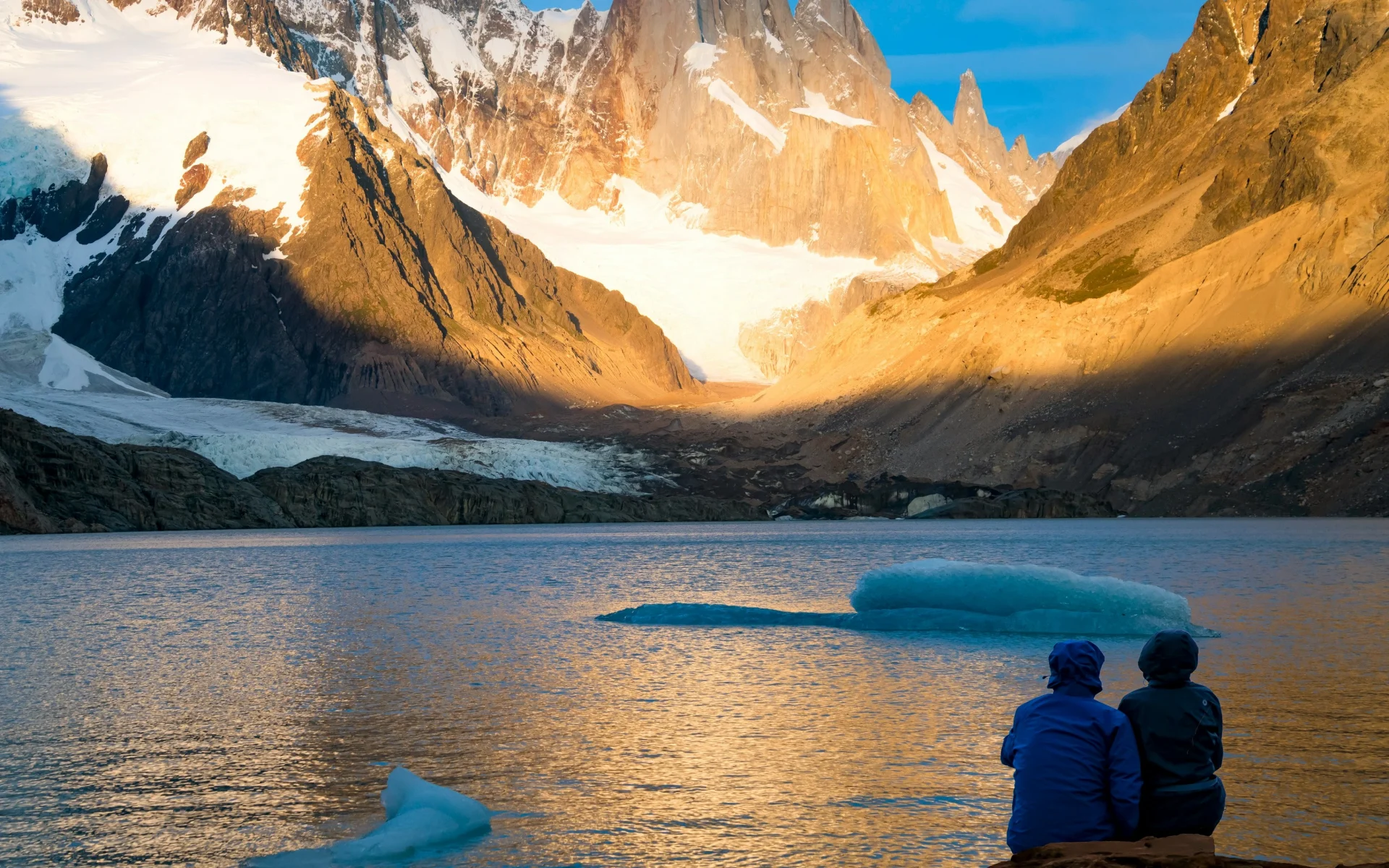 Two people sit on a rock looking out to the massive snow-capped hills of Glaciares National Park.