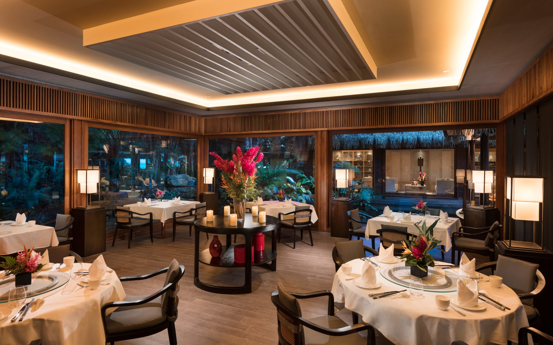 The restaurant has an elegant design with white-clothed tables and floor-to-ceiling windows. 