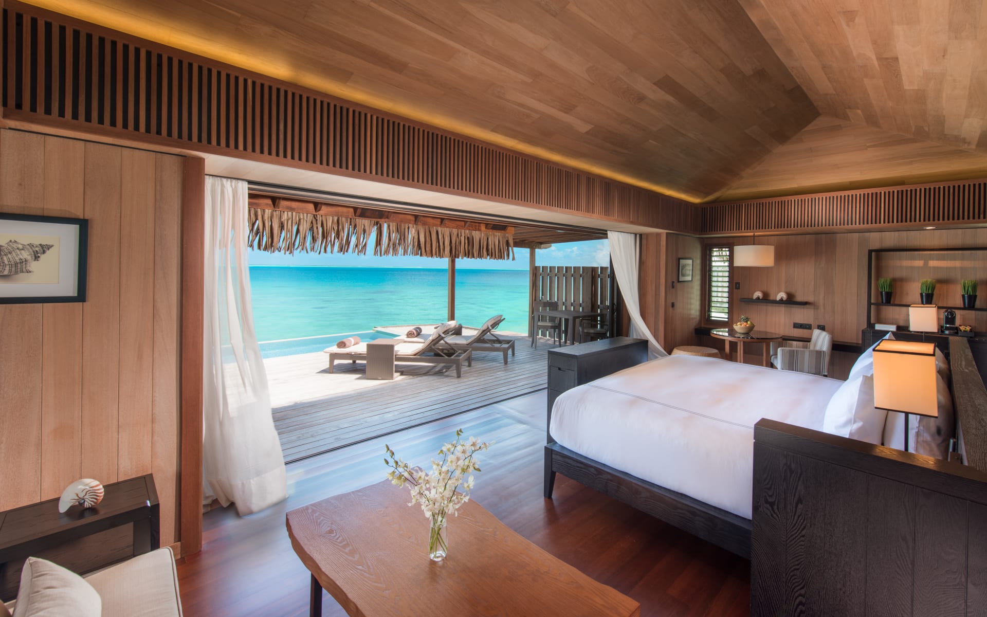 A bedroom has an open-plan design, with the room opening up to the beach. 
