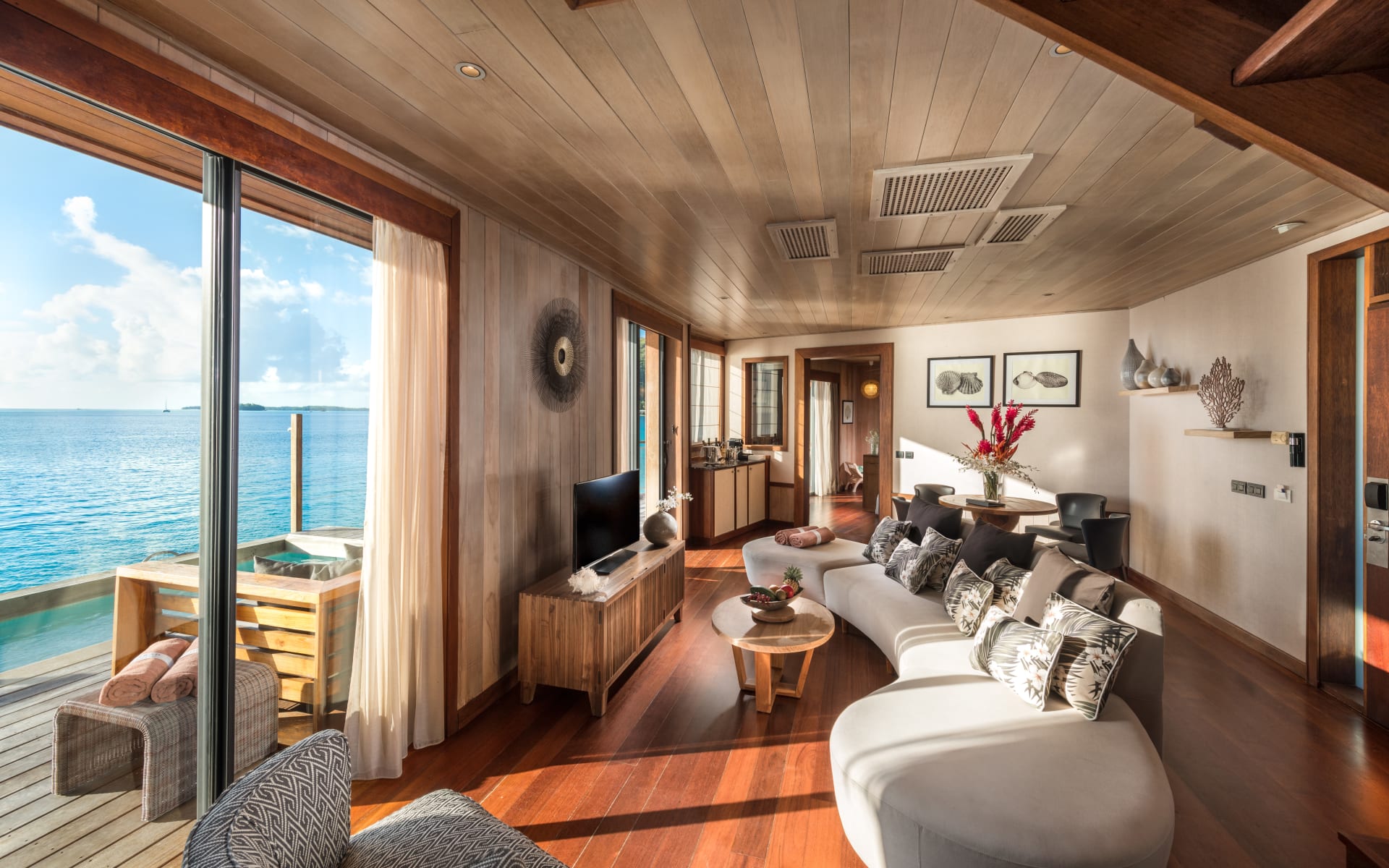 The living room has a large sofa and floor-to-ceiling windows opening up to the ocean. 