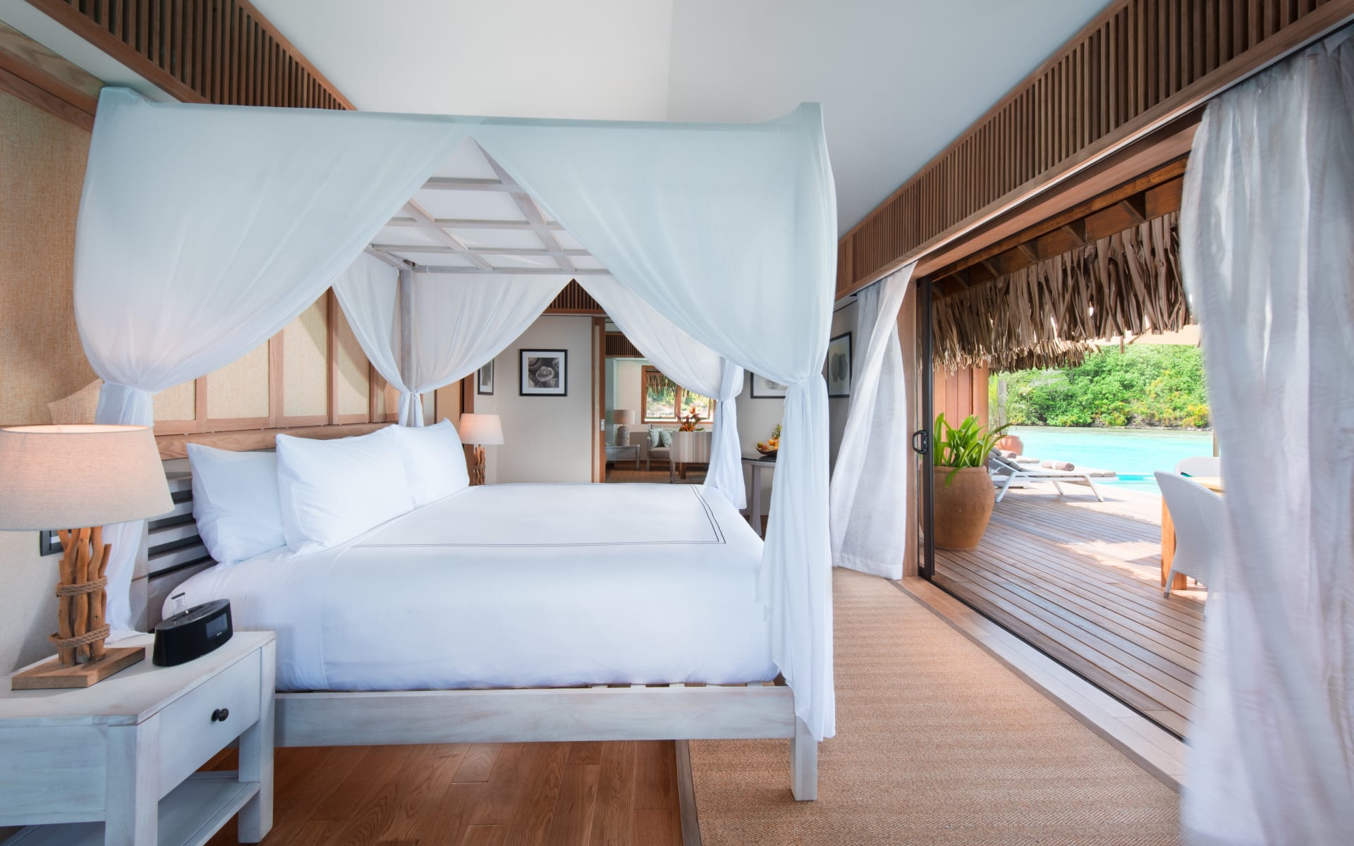 A white canopy bed sits in the middle of a room opening to a deck. 