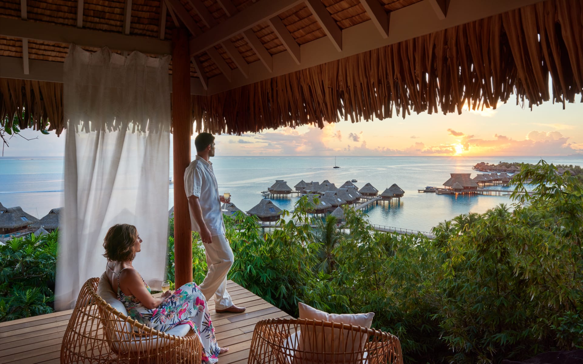 A couple is sitting on a deck looking at the overwater villas. 