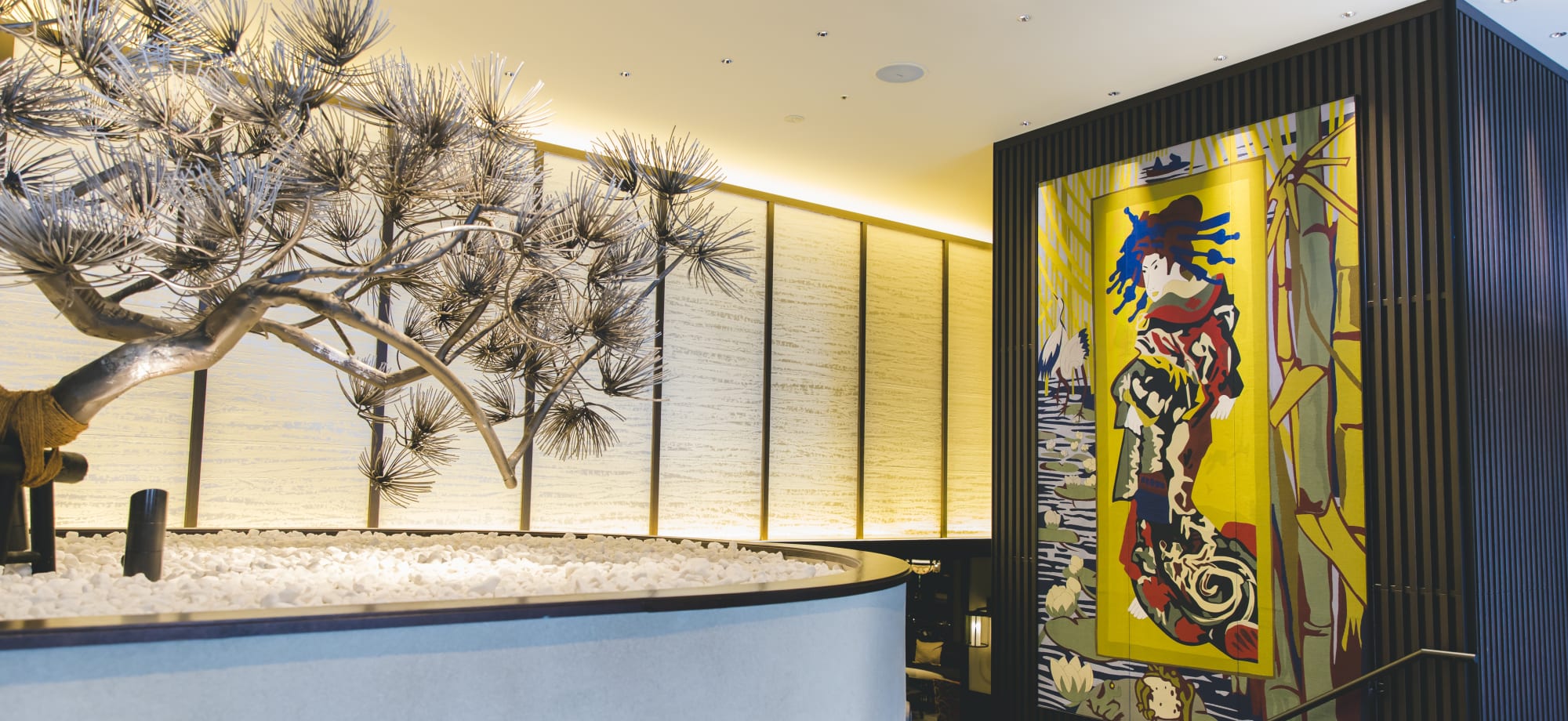 The entrance to Dhawa Yura Hotel in Kyoto has a tree and a large yellow painting of a Japanese woman. 