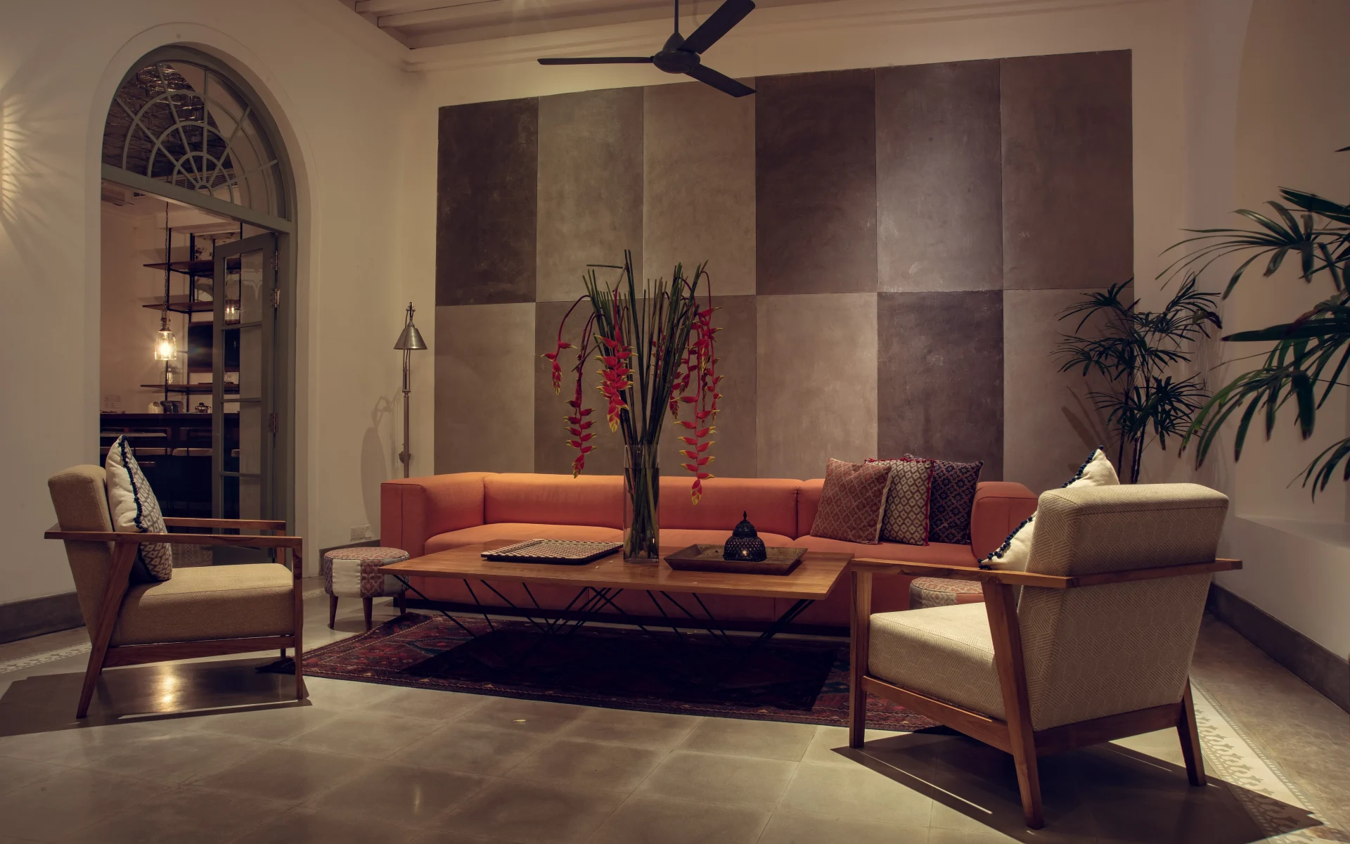 The hotel lobby is dressed in a neutral colour palette, accented by splashes of orange and red tones. There is a large sofa and two arm chairs.