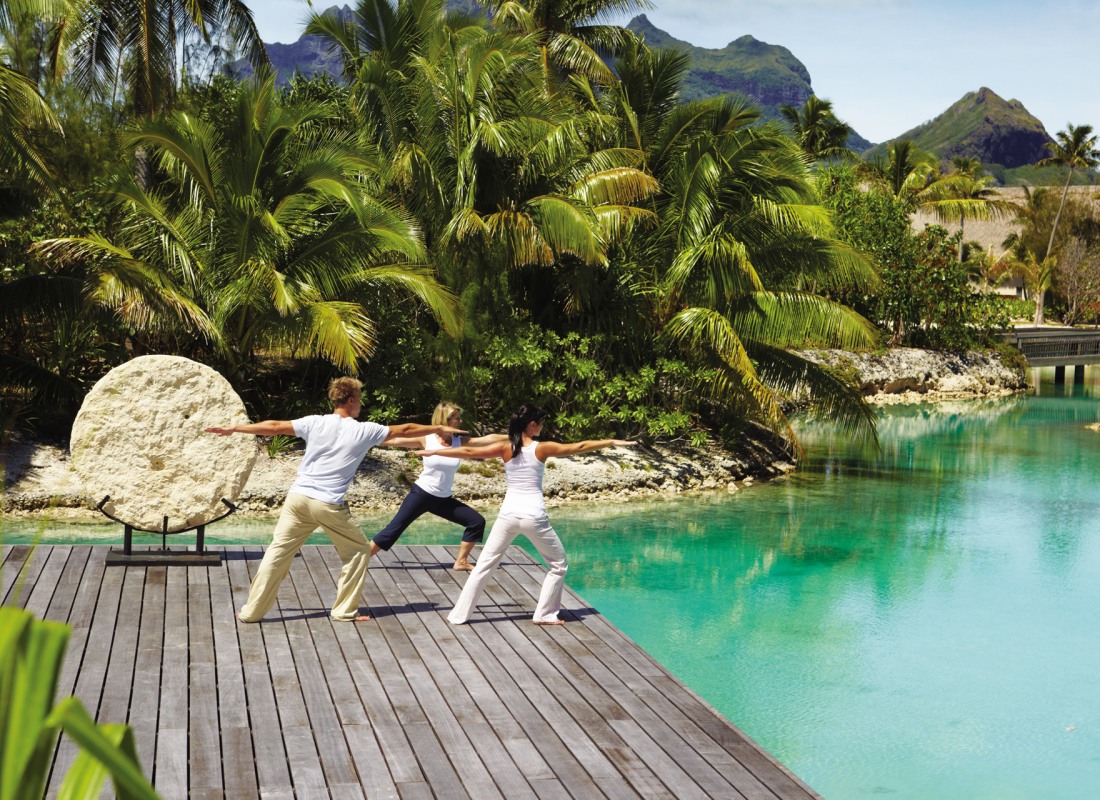 Couples yoga on deck in front of a blue lagoon