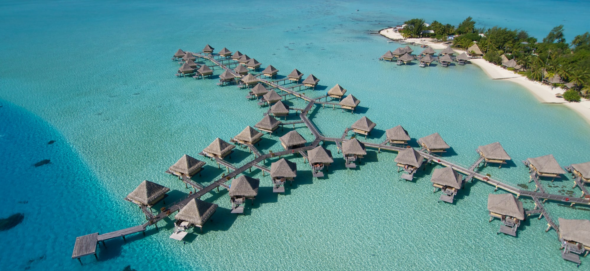 Overwater villas sit in the ocean and are backed by an island. 