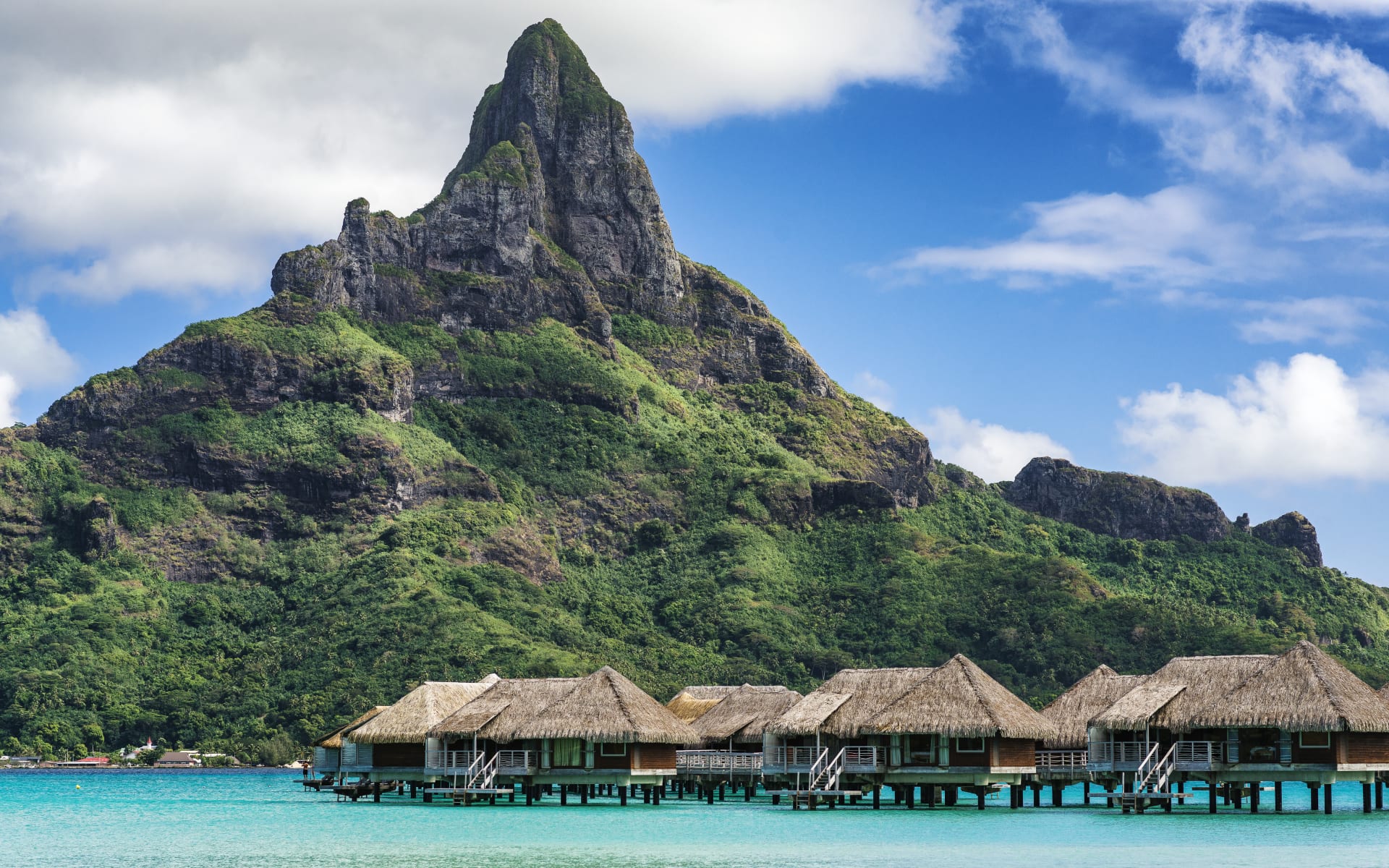 Overwater villas are surrounded by large mountians. 