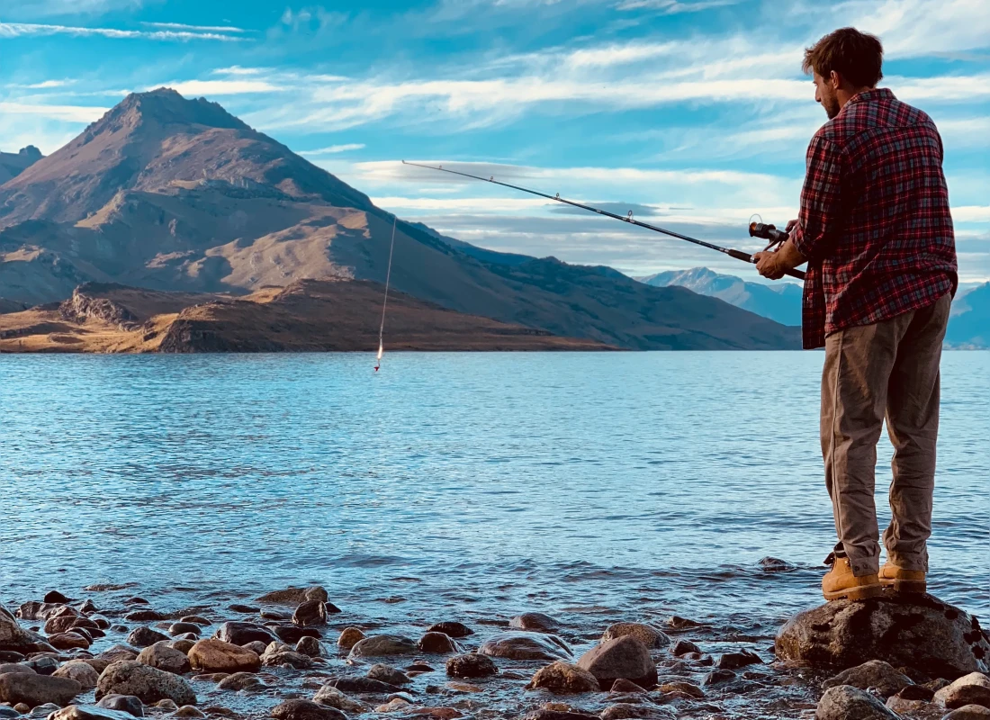 A man is fly fishing in Lake San Martin on a beautiful sunny day. The Andes Mountains rise ahead of him.