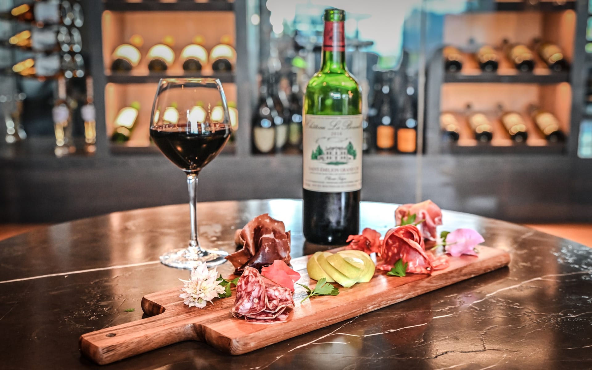 A charcuterie board has ham and cheese and is paired with a glass or red wine.