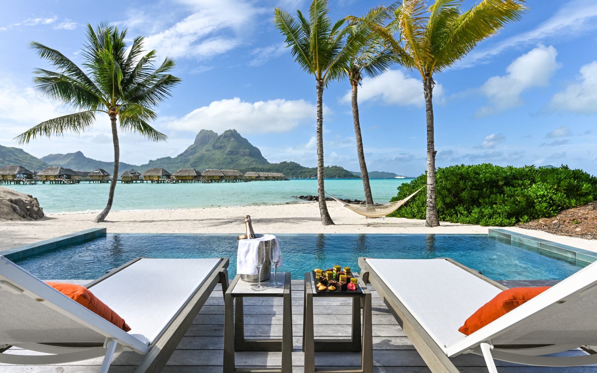 An infinity pool has two sun loungers and champagne and overlooks the ocean. 