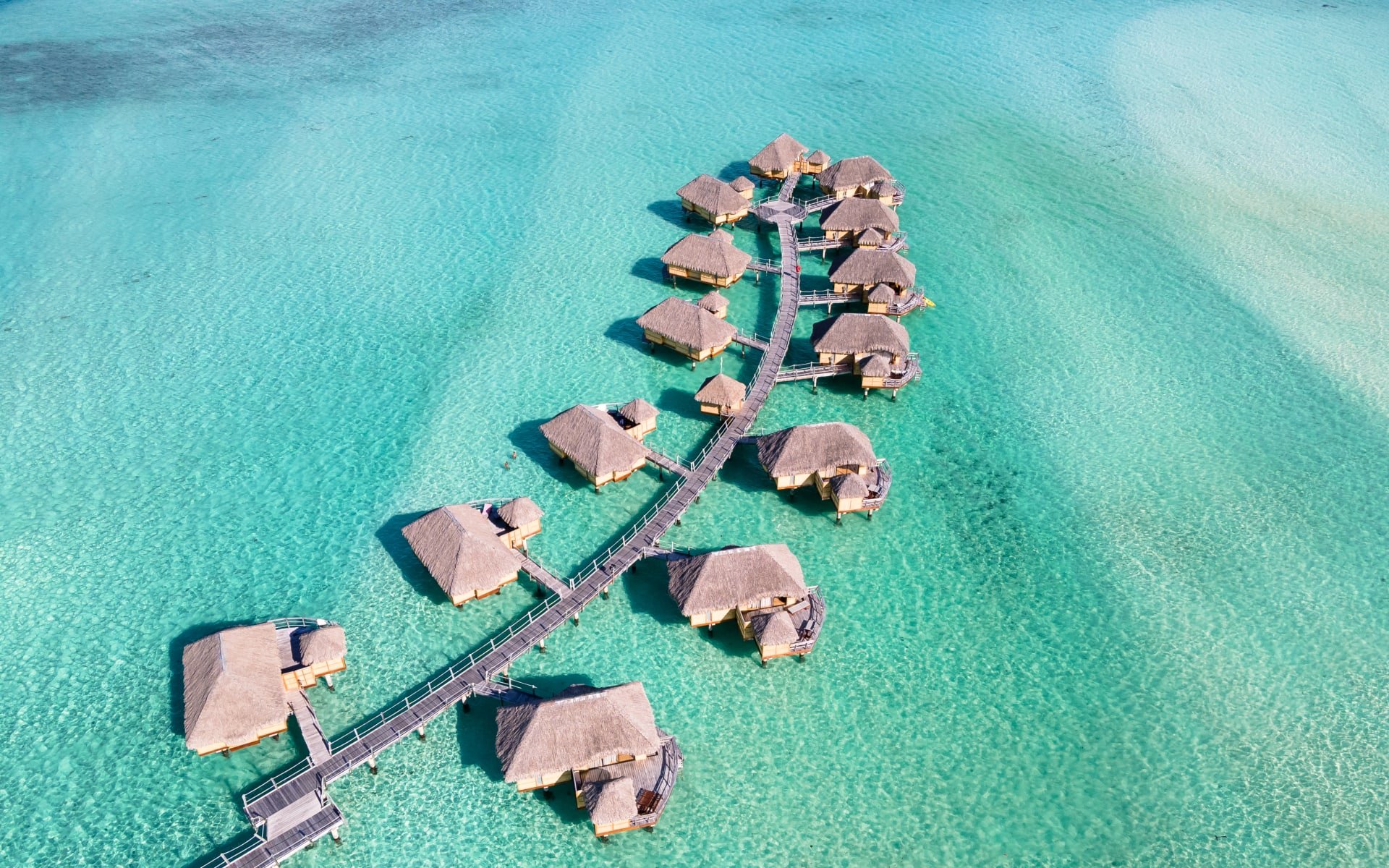 An aerial view of overwater villas that sit above a turquoise ocean.