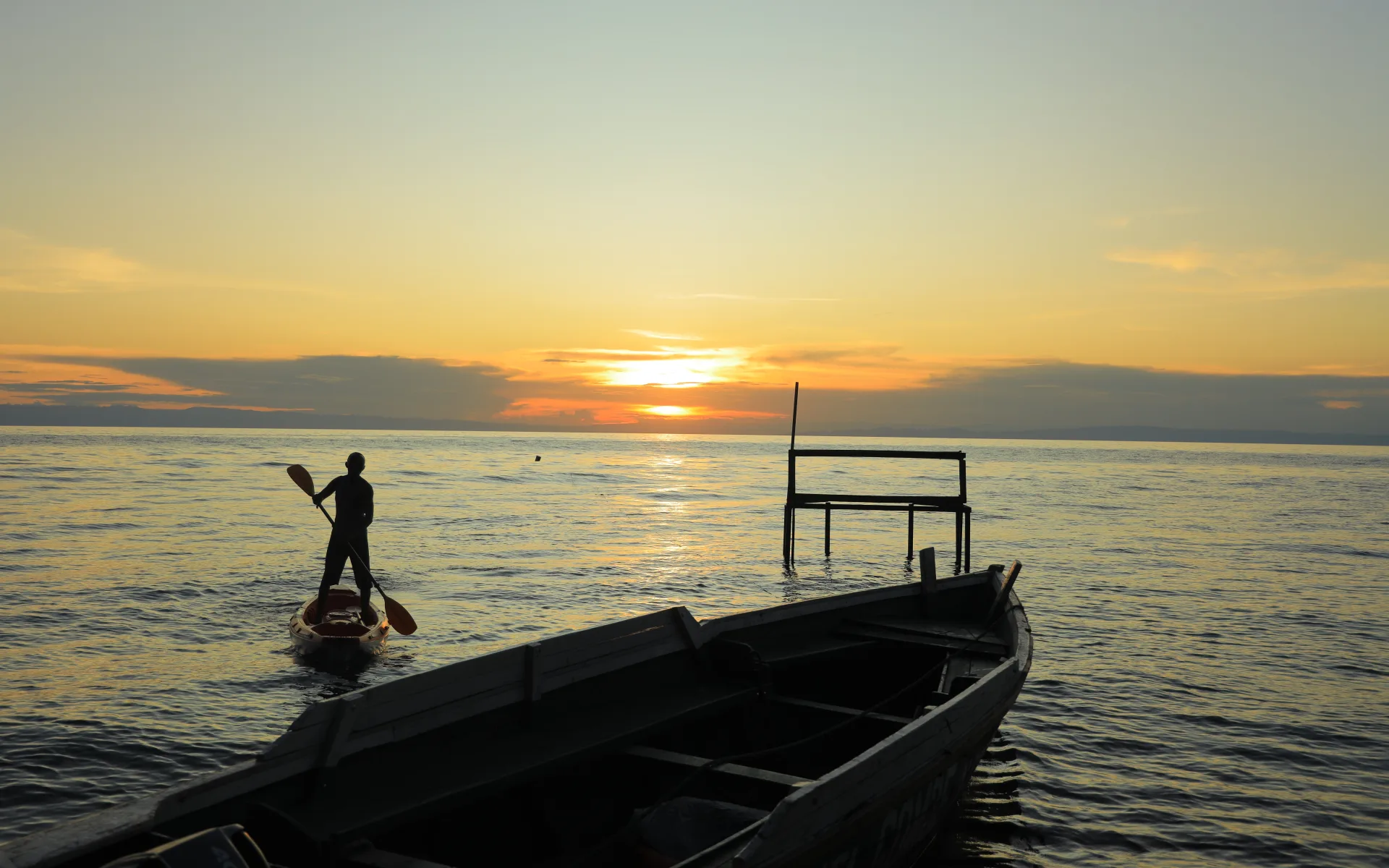 A man rows a paddling board out into Lake Tanganyika in Mahale Mountains National Park during a gentle sunset.