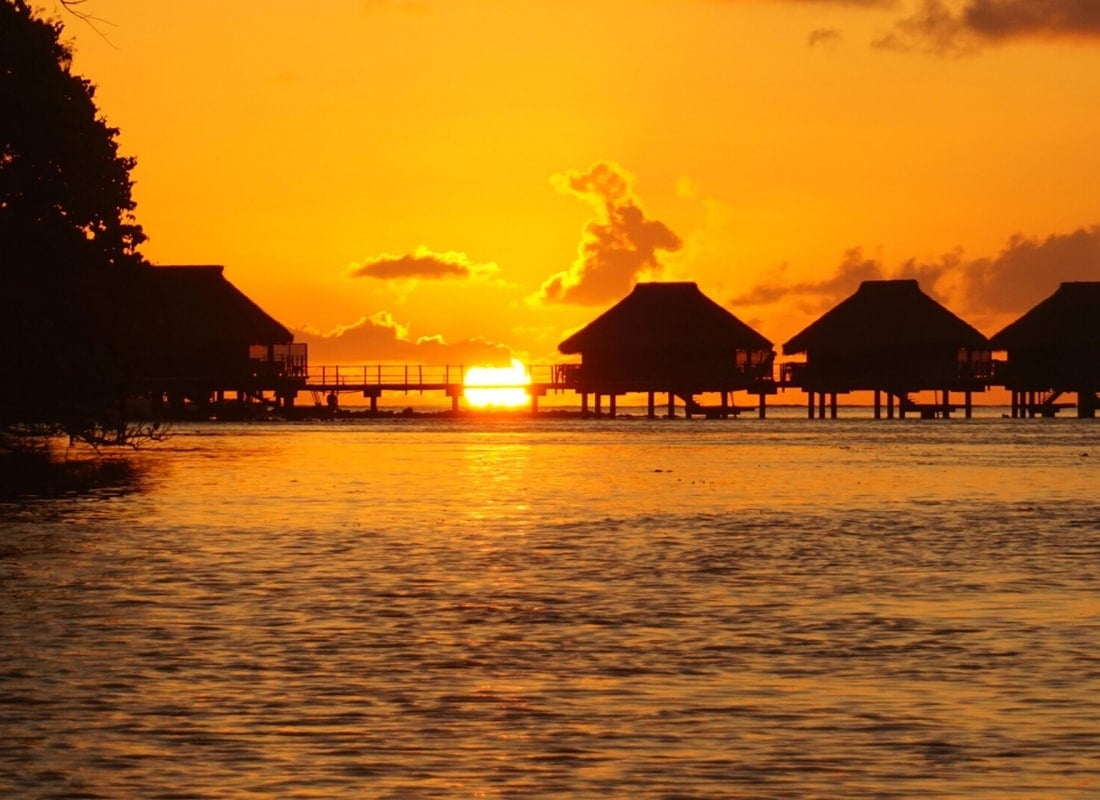 Overwater villas around surrounded by the sea and setting sun.