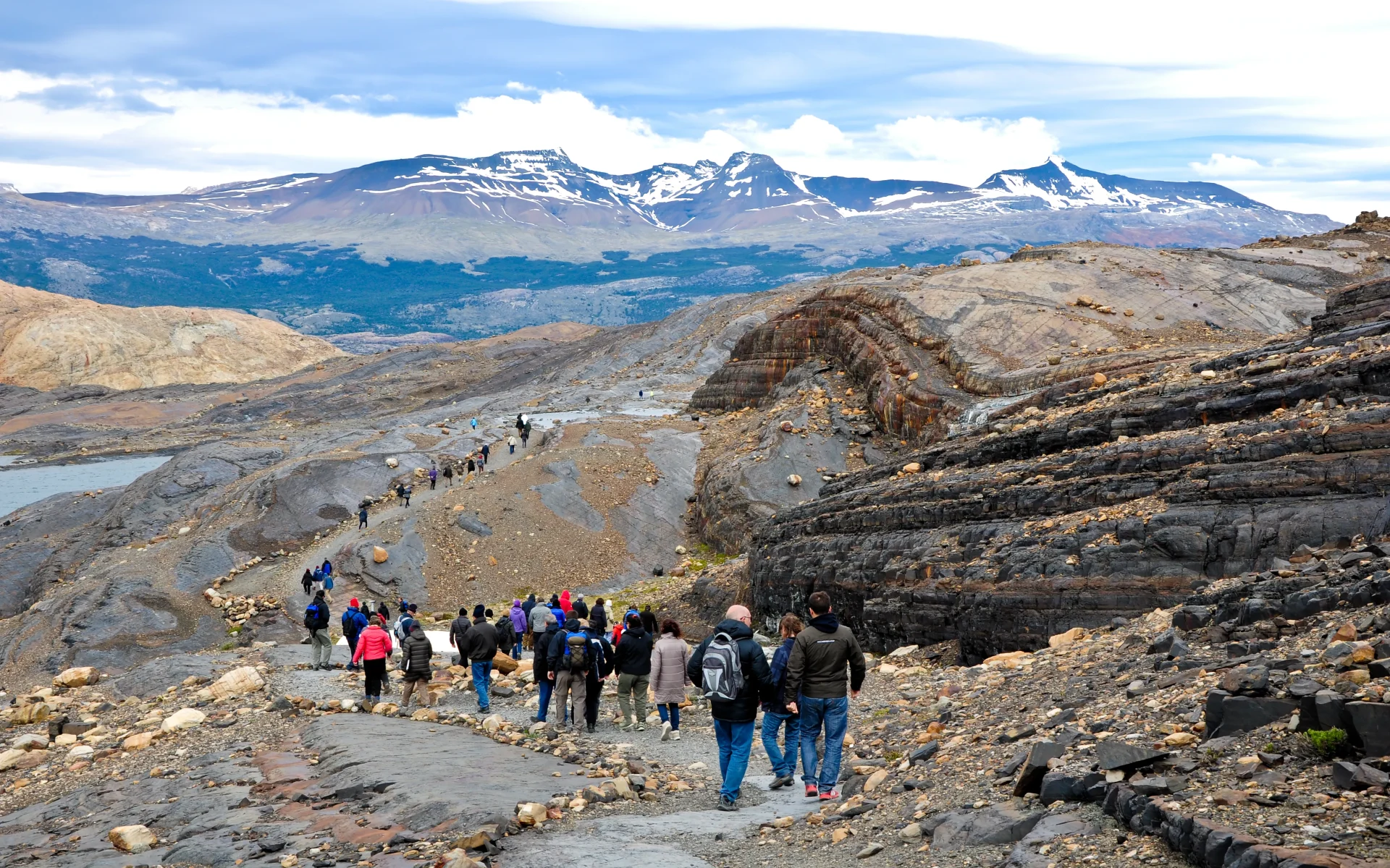 A group of people are out on a walking excursion leading down a rocky pathway towards a beautiful mountain scenery.