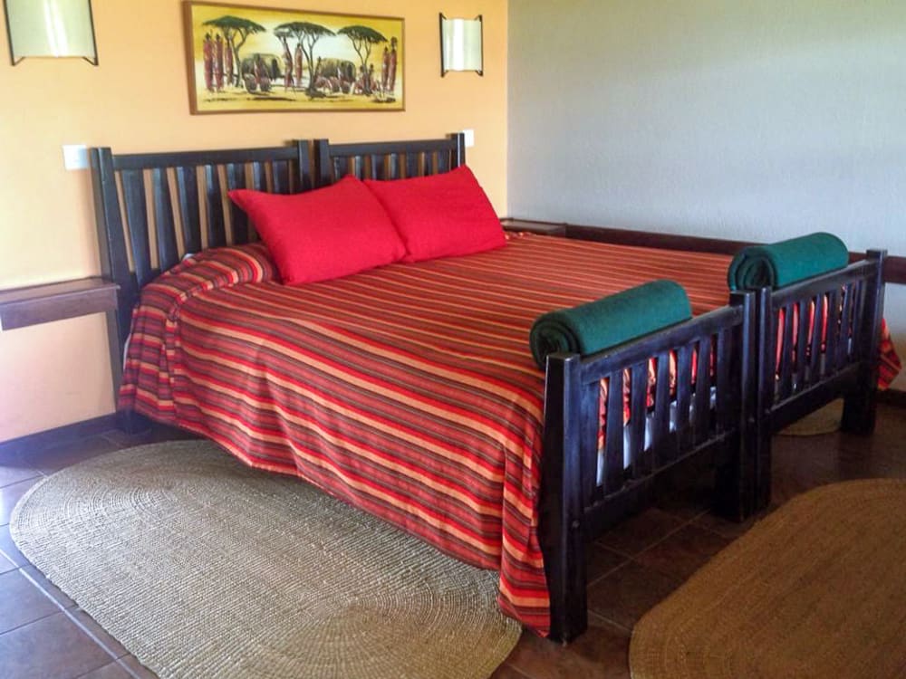 A colourful bed with red pillows and African pictures above