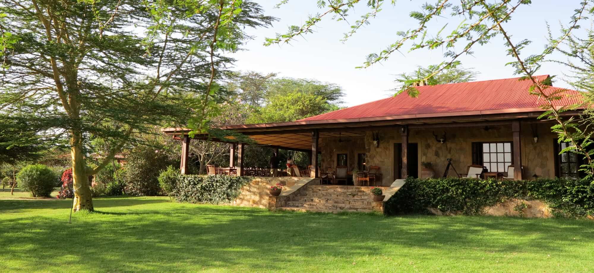 The exterior of Sosian Lodge in Kenya overlooks a green lawn. 