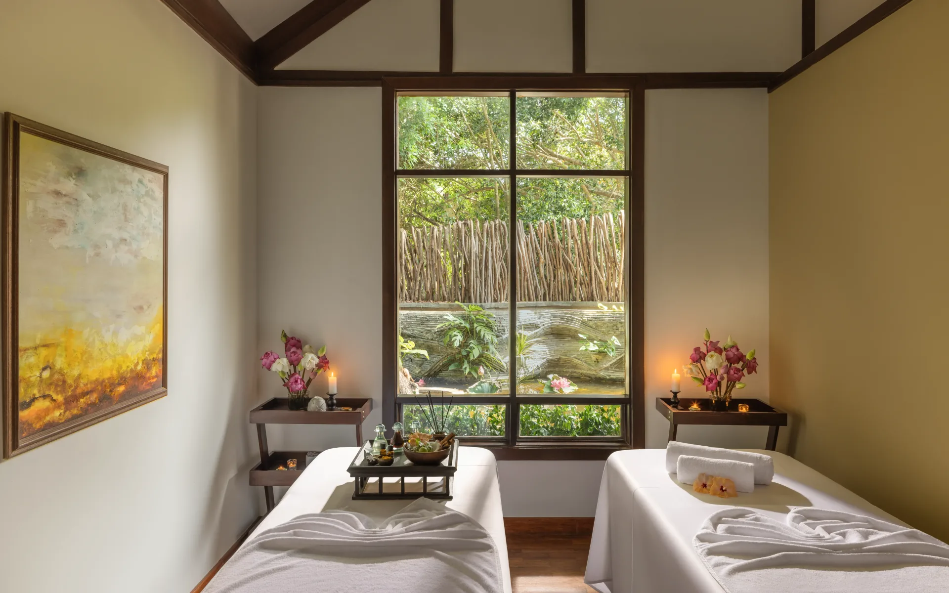 Two massage beds lay in a cosy room. A large window on-looks the surrounding jungle.